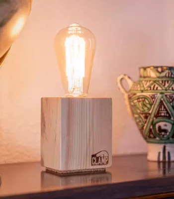 Lámpara Nara encendida, con base cúbica de madera clara, sobre una estantería junto a un globo terráqueo y una pieza de cerámica artesanal.