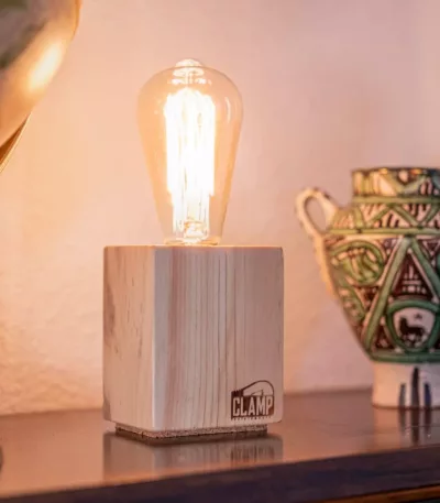 Lámpara Nara encendida, con base cúbica de madera clara, sobre una estantería junto a un globo terráqueo y una pieza de cerámica artesanal.