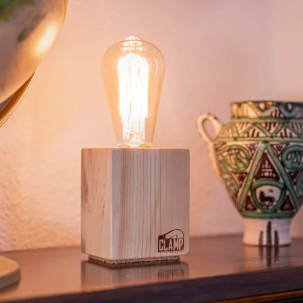 Lámpara Nara encendida, con base cúbica de madera clara, sobre una estantería junto a un globo terráqueo y una pieza de cerámica artesanal.