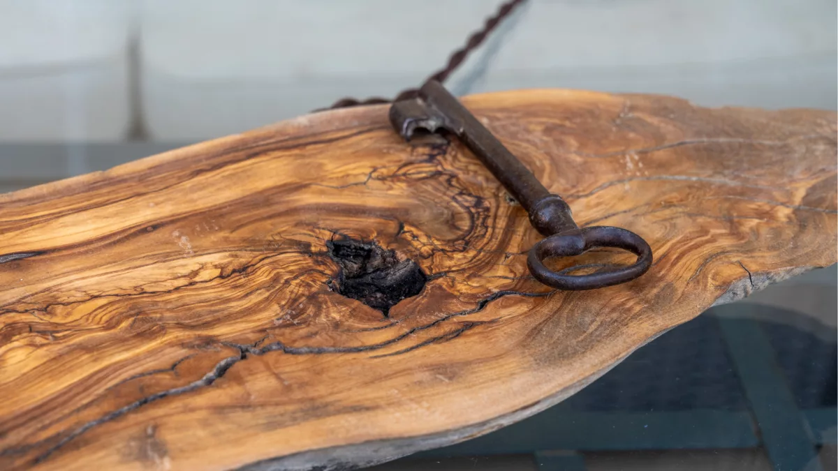 Primer plano de una base de madera natural con vetas marcadas y una llave antigua de hierro como elemento decorativo.